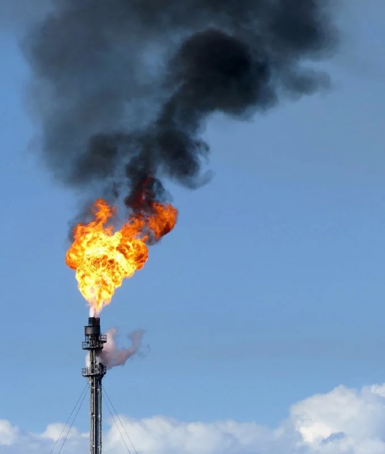 An inefficient gas flare burning orange with heavy black smoke rising from the flare tip